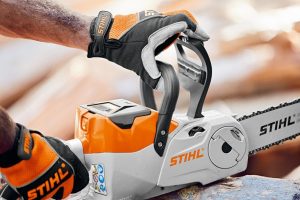 Les mains d'un travailleur avec des gants saisissent une tronçonneuse à batterie