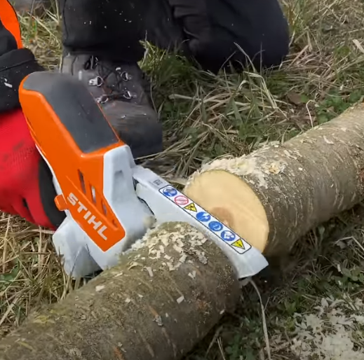 Un jardinier tronçonne une branche d'arbre en 2 morceaux avec la mini tronçonneuse stihl